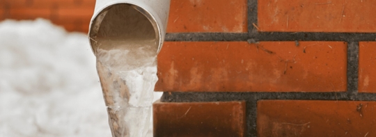 Frozen water dripping from a pipe onto bricks.