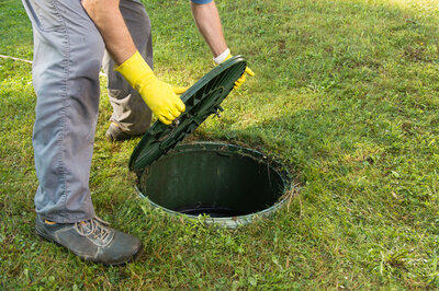 A person wearing yellow gloves removing a septic access riser cover