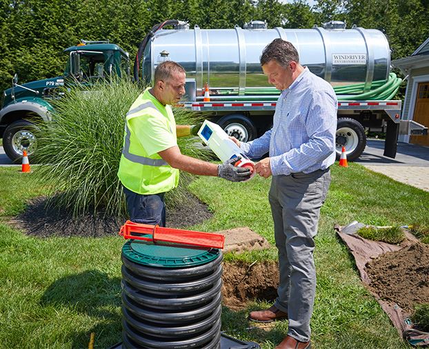 A Wind River Environmental technician handing a white septic tank filter to his client