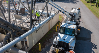 Technicians in yellow safety jackets using a vacuum truck to clean a lift station