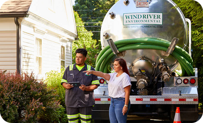 Wind River Environmental technician talking with a homeowner outside her home, with a pumping truck in the background