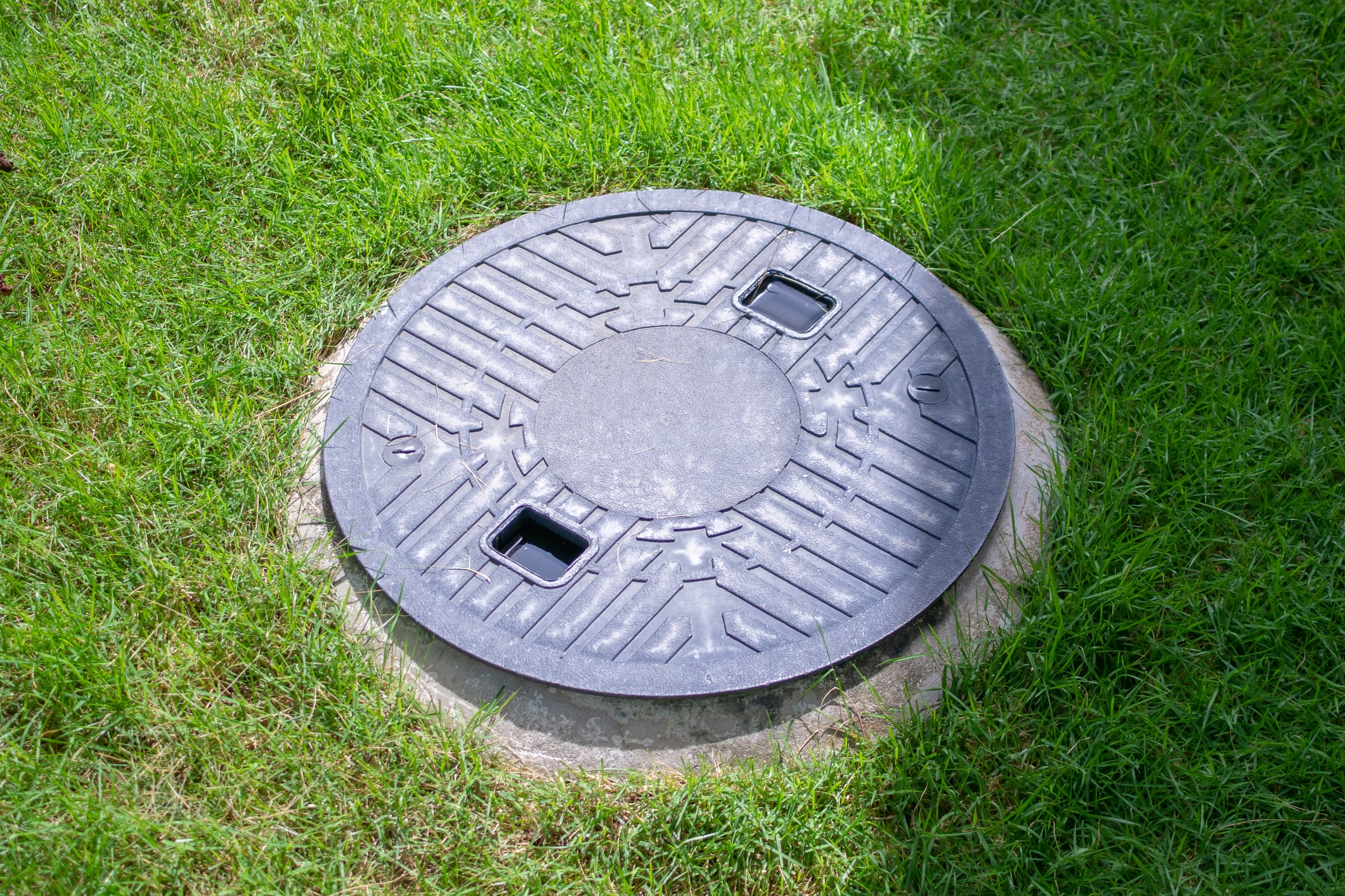 Closed round septic tank lid set flush with grass, covering the septic tank filter access point.
