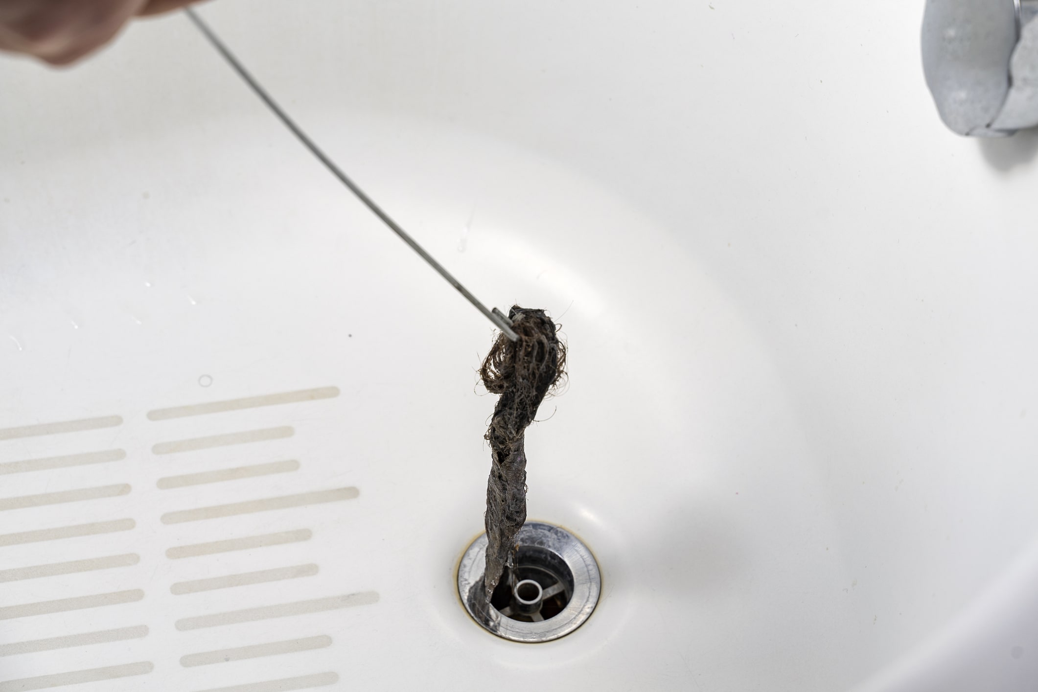 A wire hanger pulled from a bathroom sink drain, removing a clump of debris during a clog removal.